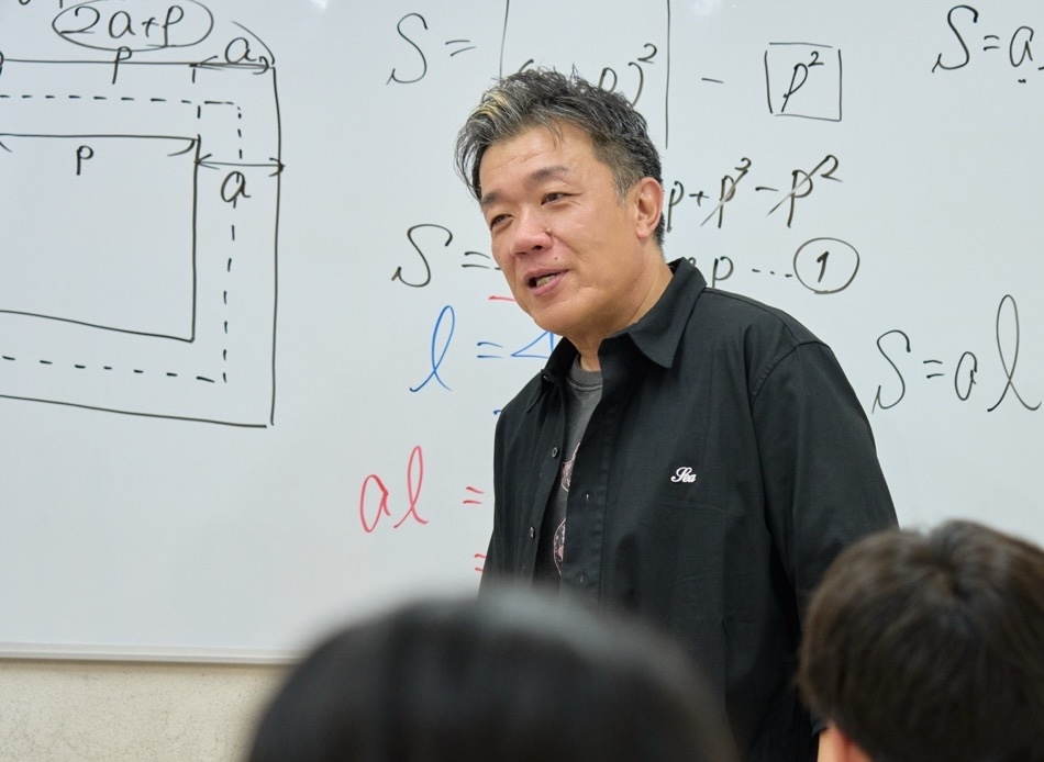 塾長が生徒の後ろ姿を前に数学を説明している教室風景